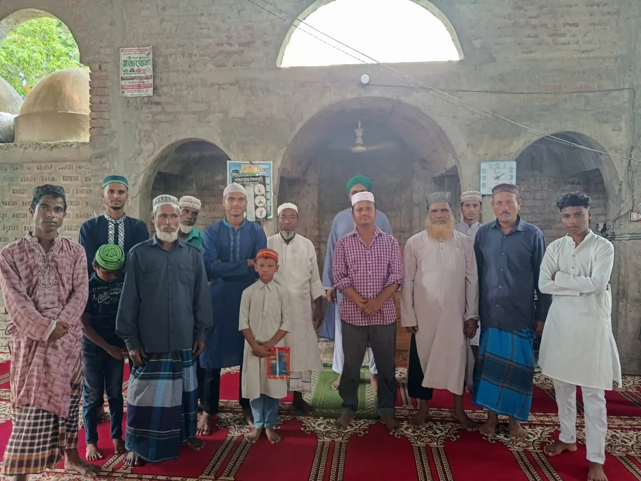 A group of men and boys standing together inside a mosque with arched brick walls
