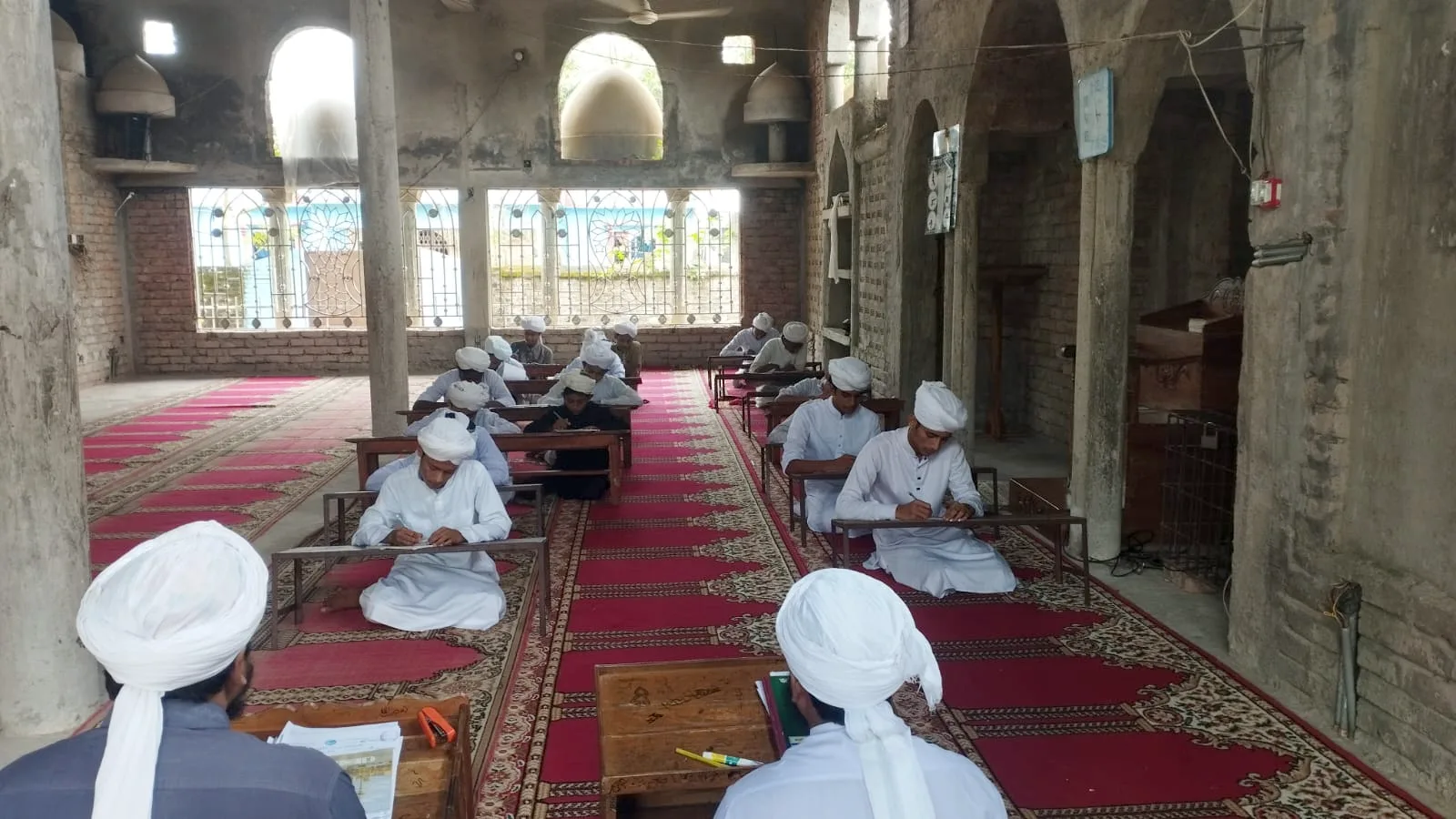Students writing at desks in a long mosque hall
