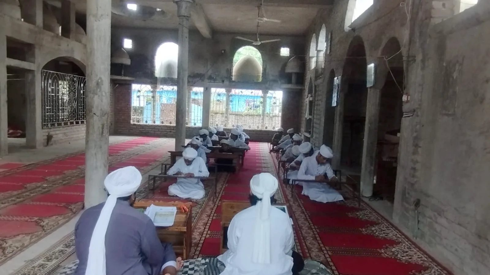 A wide view of students studying at desks in a mosque hall