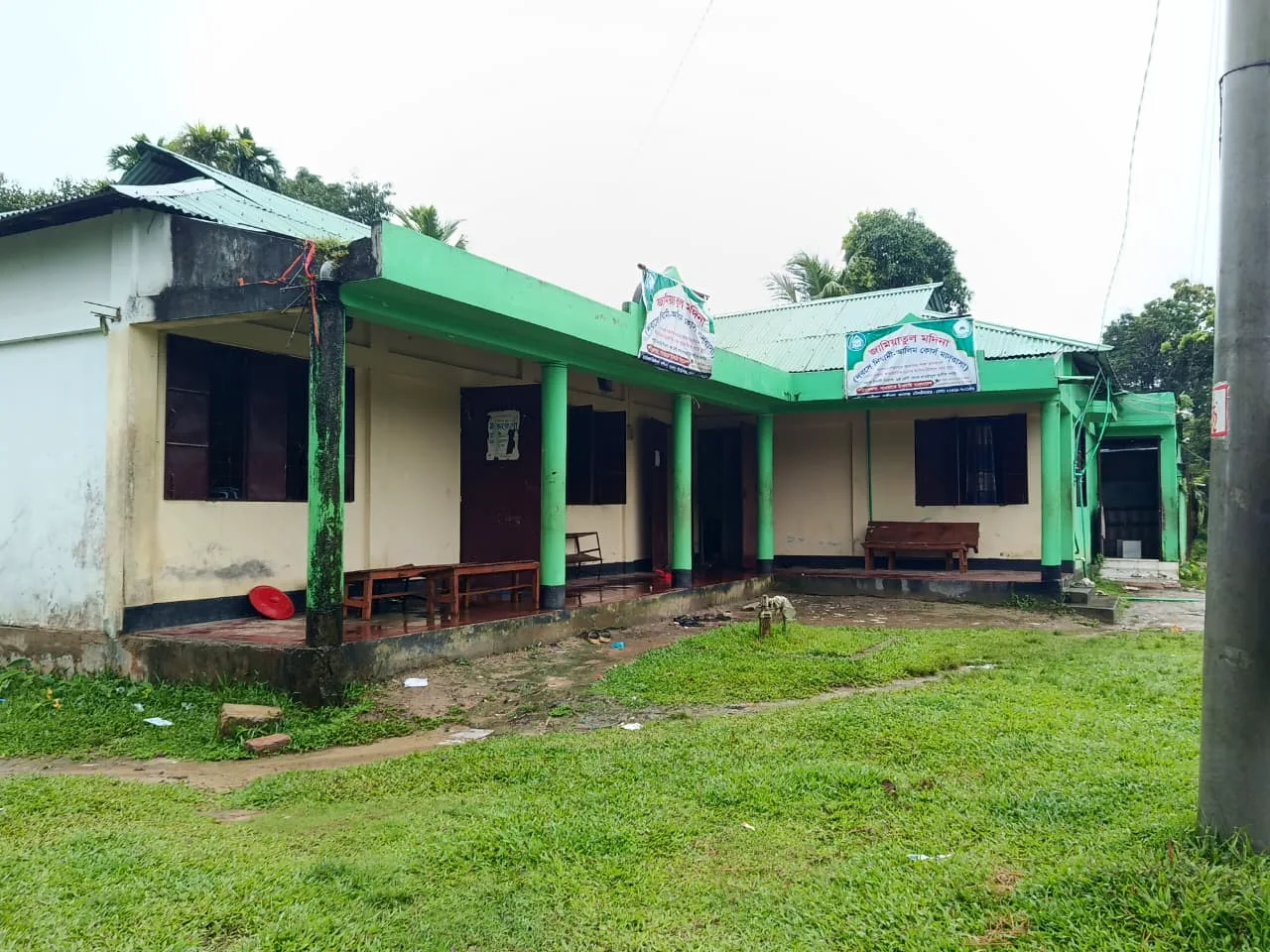 A single-storey building with green pillars and banners, with a lawn in front