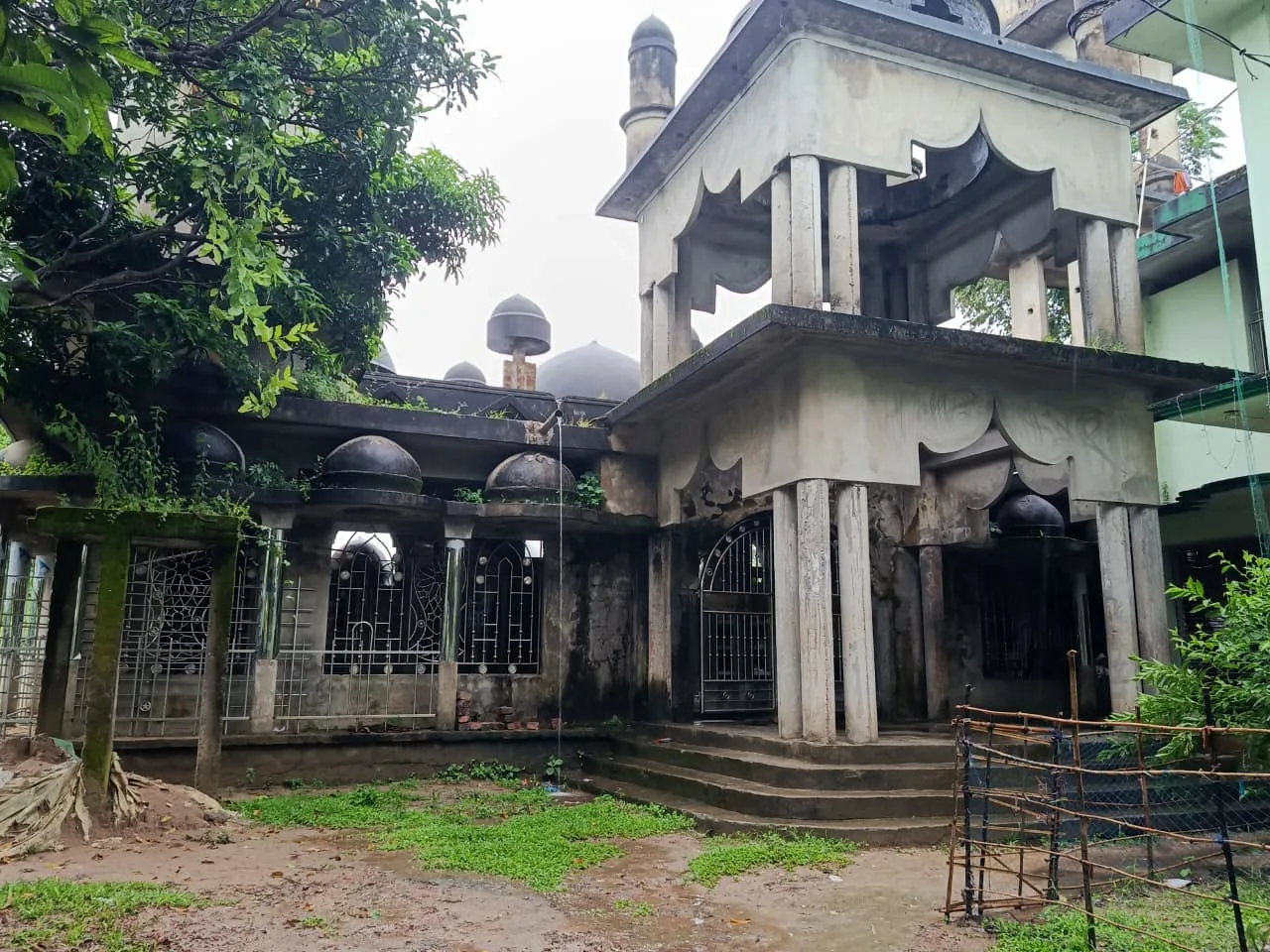 A weathered mosque with domes and a two-tier gateway in daylight