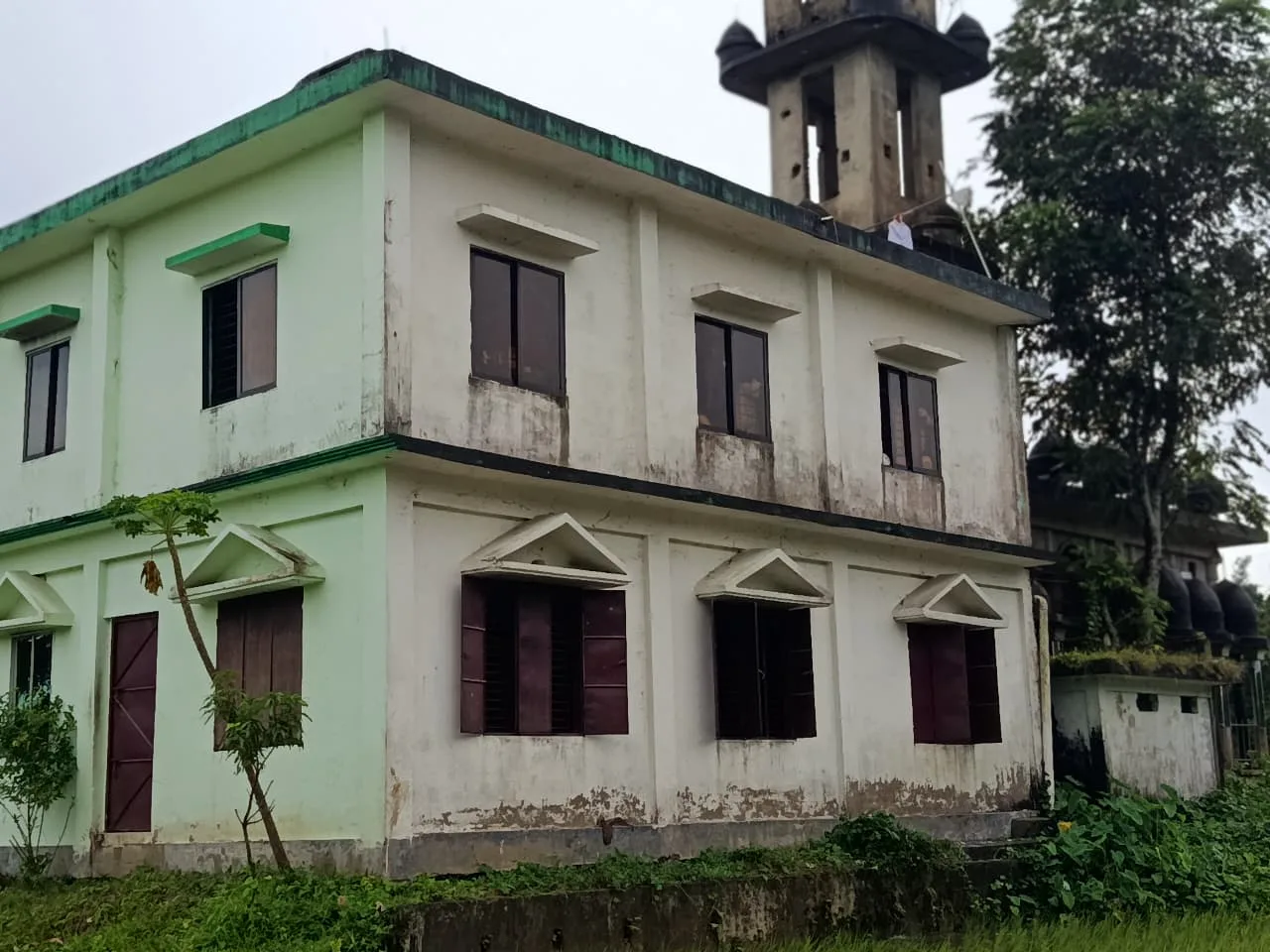 A two-storey pale green and white building with a minaret behind it