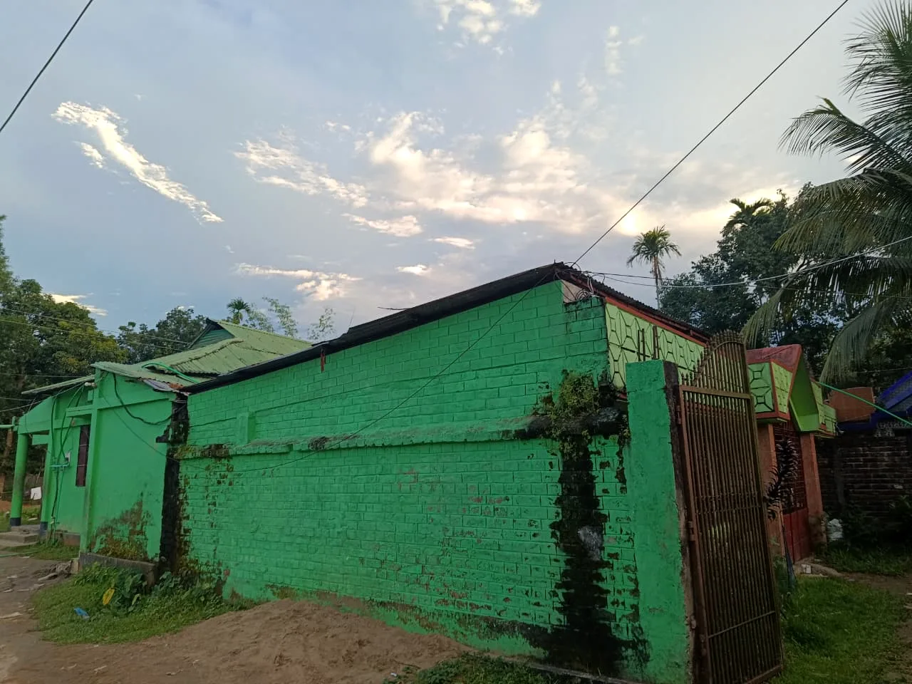 A green-painted brick building and gate under an evening sky
