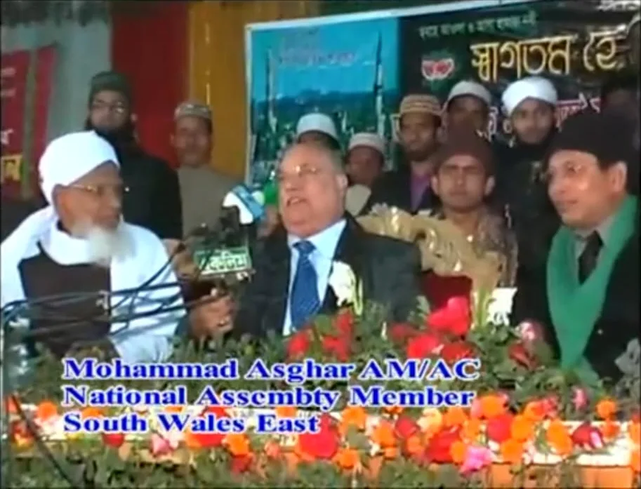 Television footage of the same speaker seated with other guests, captioned Mohammad Asghar AM